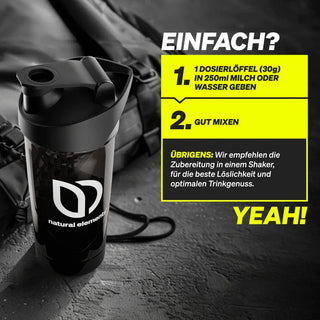 Eine schwarze Shaker-Flasche mit dem "natural elements"-Logo auf einer dunklen Oberfläche, daneben eine Anleitung auf Deutsch, wie man einen Messlöffel in 250 ml Milch oder Wasser einrührt und gut schüttelt.